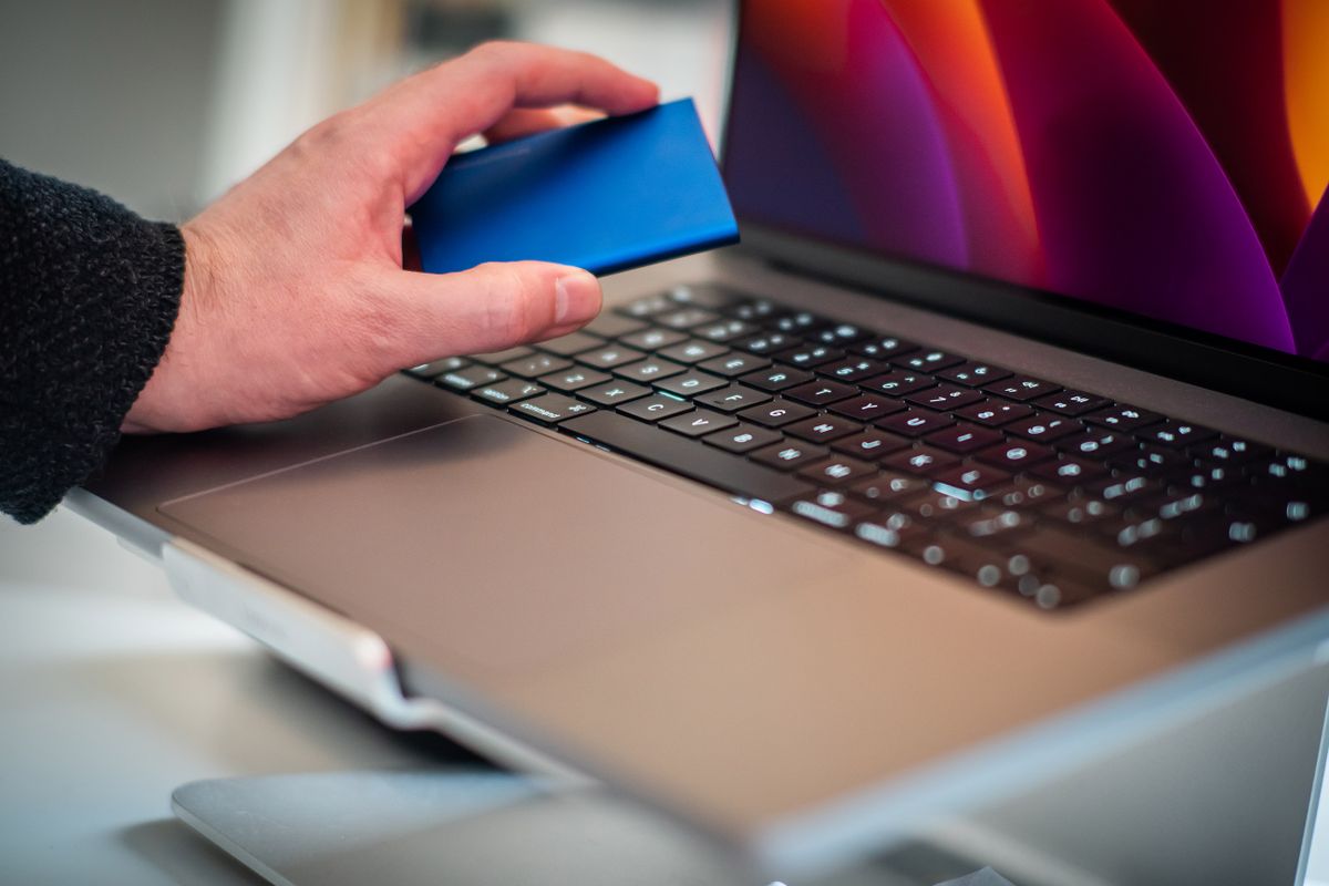 SSD esterno portatile tenuto in mano accanto a un computer portatile