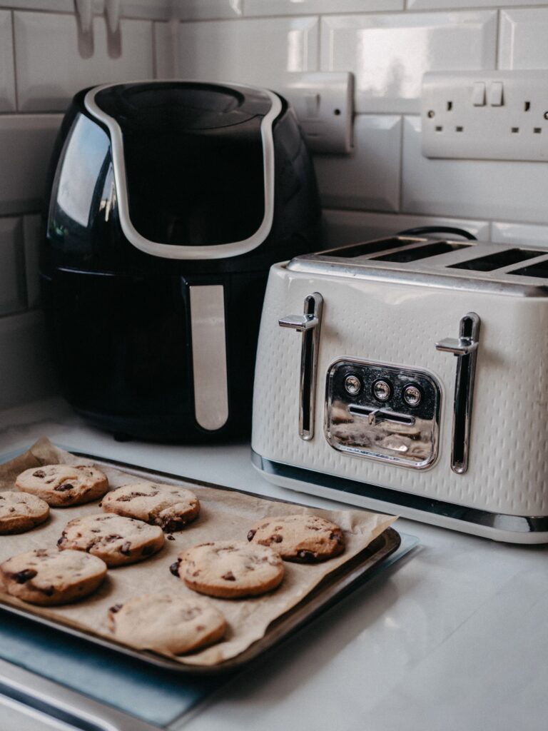 Friggitrice ad aria con vapore sul piano di lavoro di una cucina, accanto a una teglia di biscotti appena sfornati