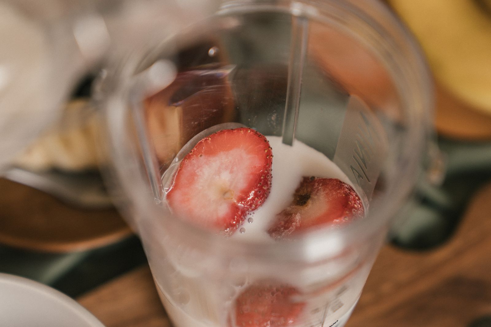 Caraffa di un frullatore vista dall’alto con fragole a fette immerse nel latte